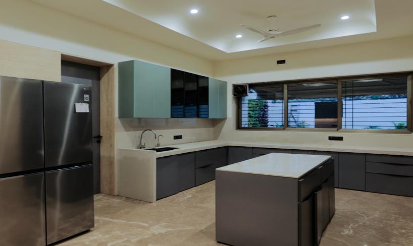 Modern kitchen with a central island, stainless-steel fridge, dark cabinetry and night windows.