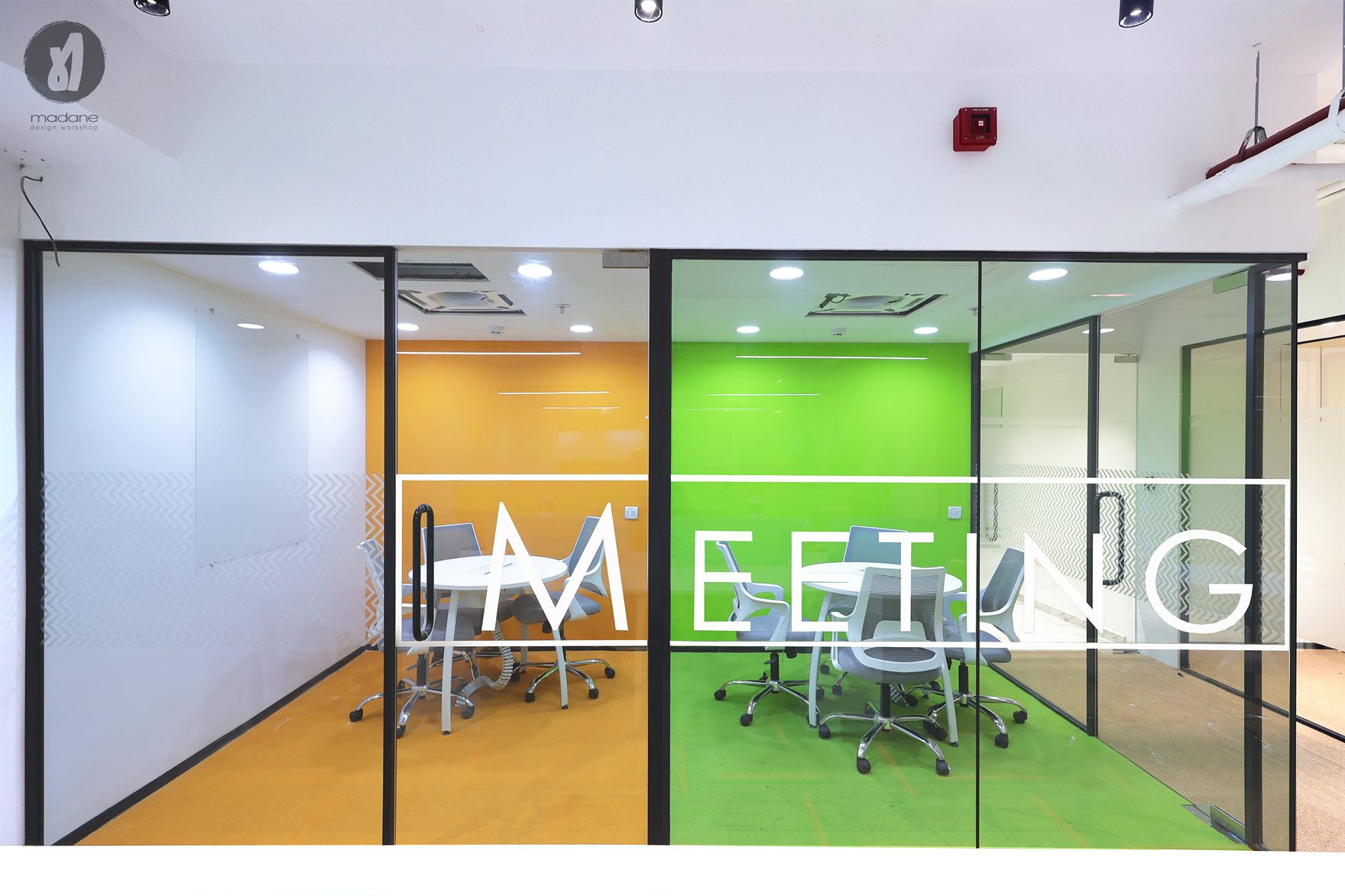 Glass-fronted meeting rooms with orange and green painted interiors and matching floor carpet, overlaid with frosted MEETING lettering