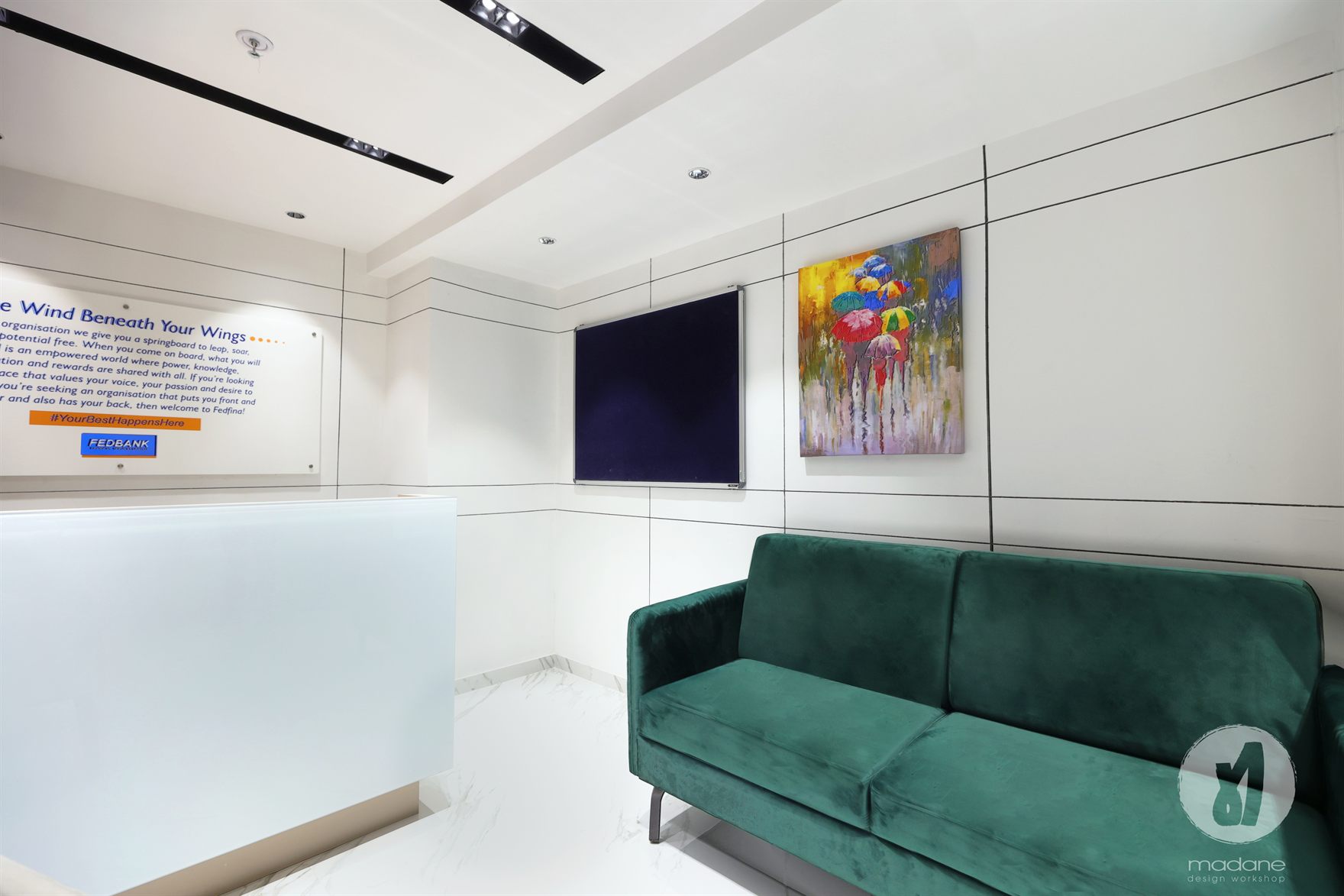 Waiting area with a green velvet sofa, colourful umbrella painting and a pin-up board on a line-jointed white wall over marble flooring