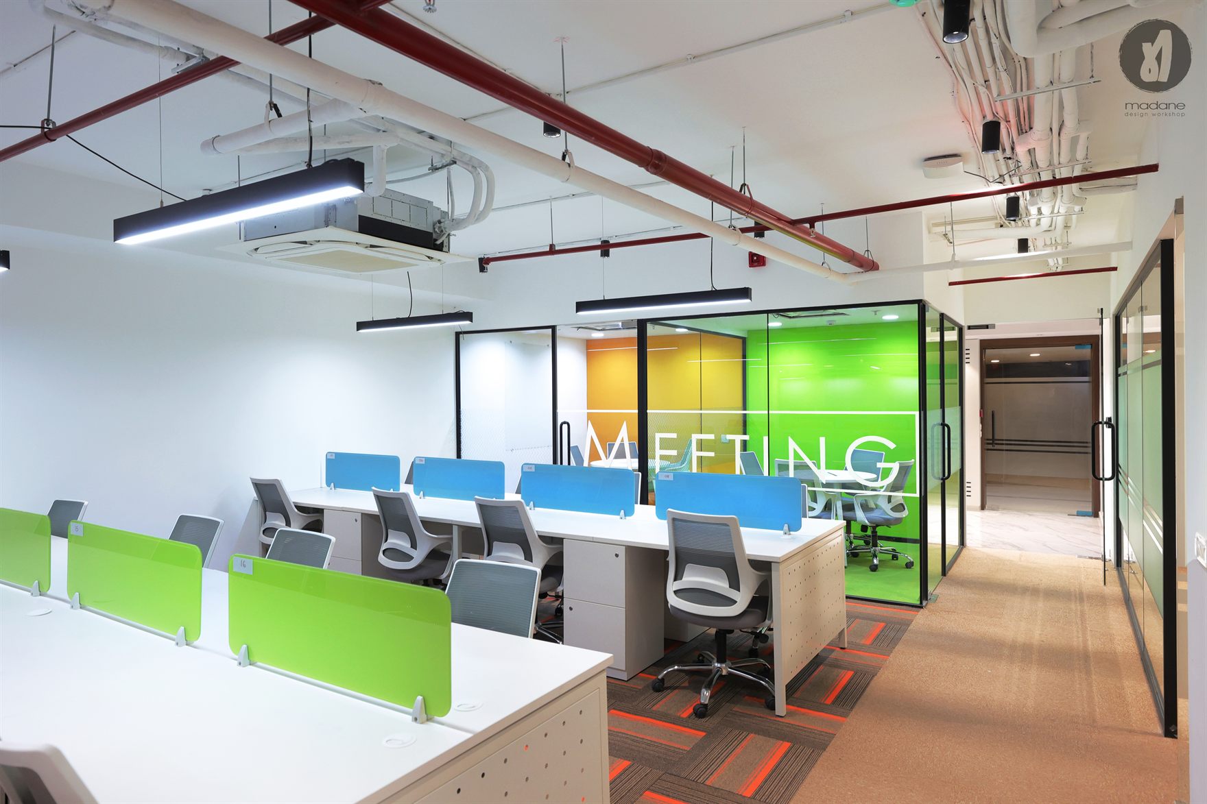 Open workstations with green desk screens facing glass meeting rooms in orange and green under exposed red and white ceiling pipes