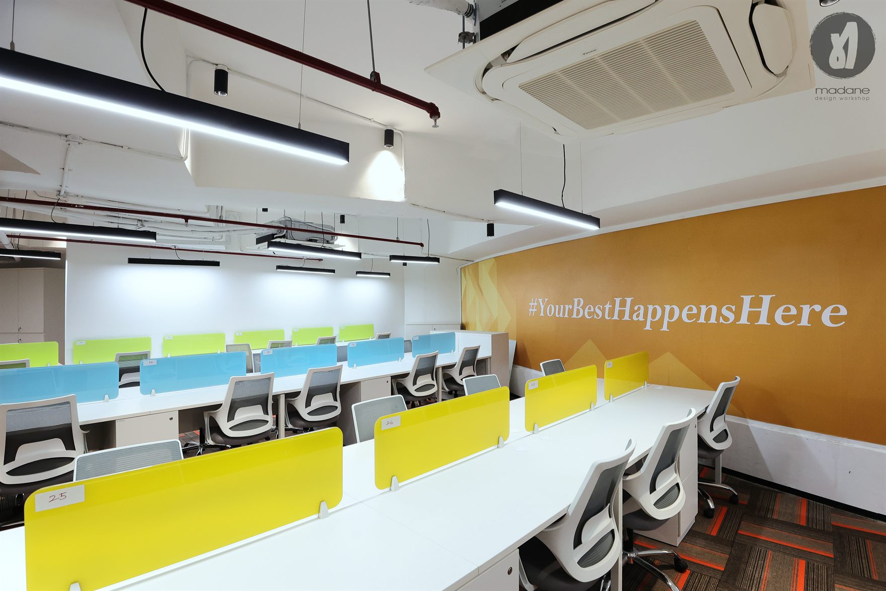 Rows of white bench desks with blue and yellow screens against an ochre wall reading hashtag Your Best Happens Here