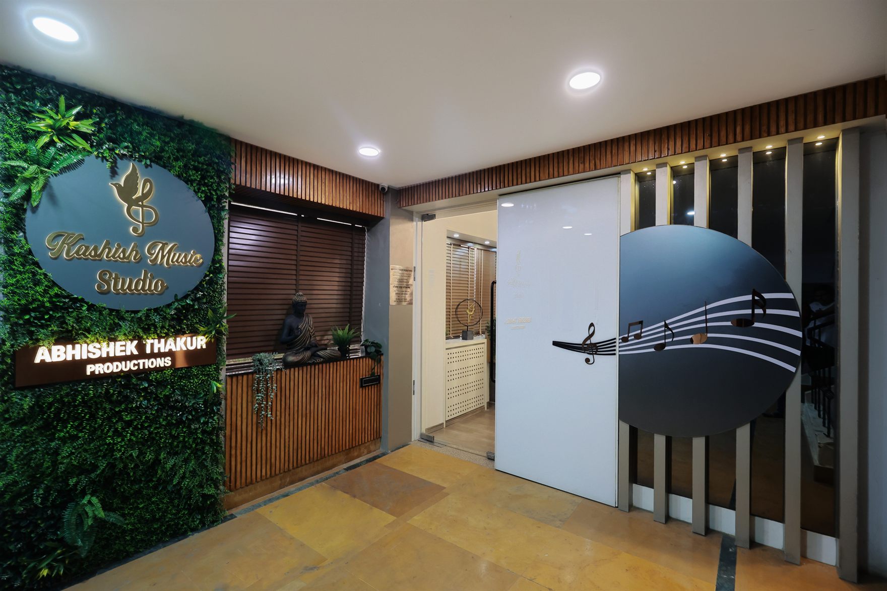 Entrance with a green vertical-garden wall carrying the Kashish Music Studio oval sign and a seated Buddha, beside a sliding door printed with musical notes over a yellow stone floor