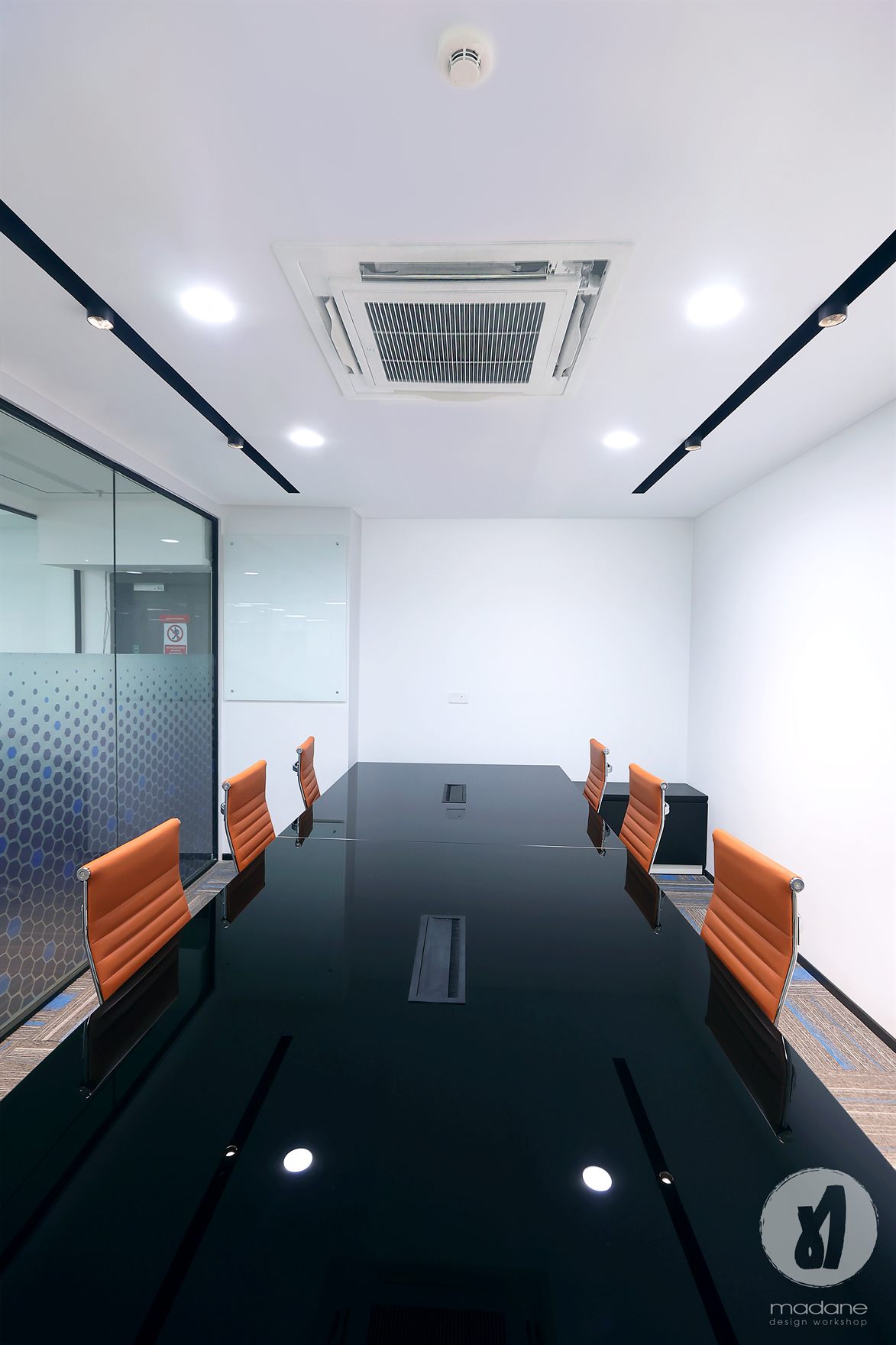 Boardroom with a glossy black table and tan leather chairs beside a hexagon-film glass wall under recessed downlights