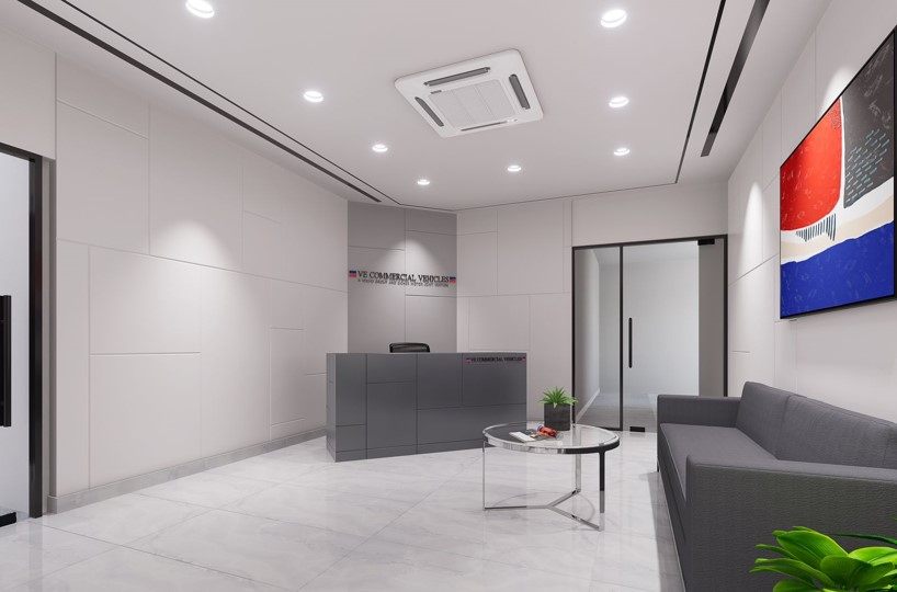 Minimal white reception with VE Commercial Vehicles signage, grey desk, cassette AC ceiling and brand-coloured wall art.